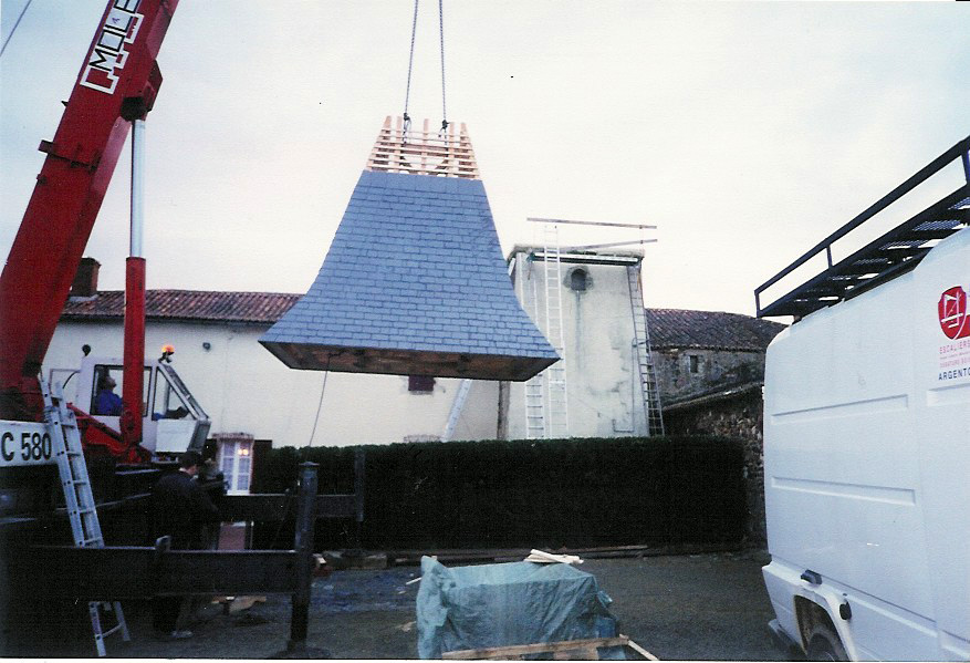 restauration patrimoine ancien tour carrée Les ¾ de la charpente ont été recouvertes d'ardoises et la toiture est soulevée par une grue pour reprendre sa place sur la tour