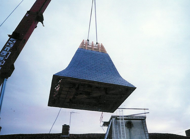 restauration patrimoine ancien tour carrée La grue continue de soulever la toiture pour la placer sur la tour